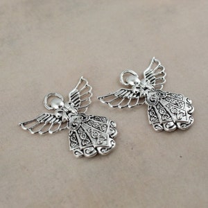 Pu&ograve; includere: Due ciondoli a forma di angelo in argento con dettagli intricati e un anello per appenderli.