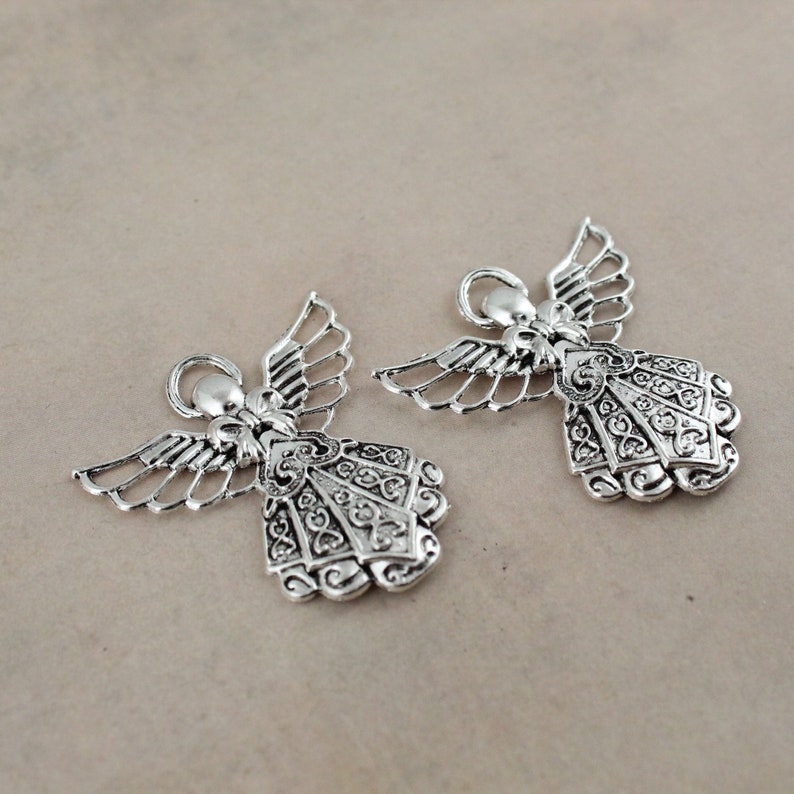 Pu&ograve; includere: Due ciondoli a forma di angelo in argento con dettagli intricati e un anello per appenderli.