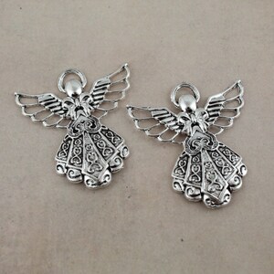 Pu&ograve; includere: Due ciondoli a forma di angelo in argento con dettagli intricati e un design a filigrana. Gli angeli tengono un arco nelle loro mani e hanno le ali.
