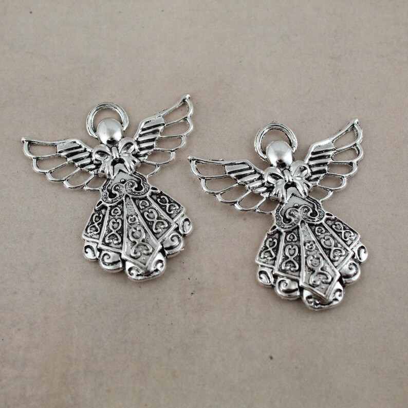 Pu&ograve; includere: Due ciondoli a forma di angelo in argento con dettagli intricati e un design a filigrana. Gli angeli tengono un arco nelle loro mani e hanno le ali.