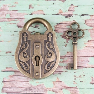 May include: An antique-style bronze padlock with ornate scrollwork and a matching key. The padlock has a rounded top and a keyhole. The key has a decorative handle. The items are set against a distressed, weathered background.