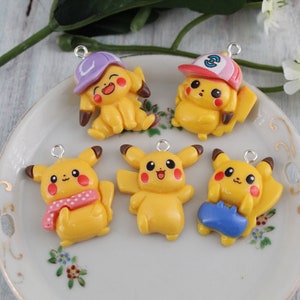 May include: Five yellow Pikachu charms with different accessories. The charms are made of polymer clay and have a shiny finish. The accessories include a purple hat, a baseball cap with the number 3, a pink scarf, a blue shirt, and a plain design.