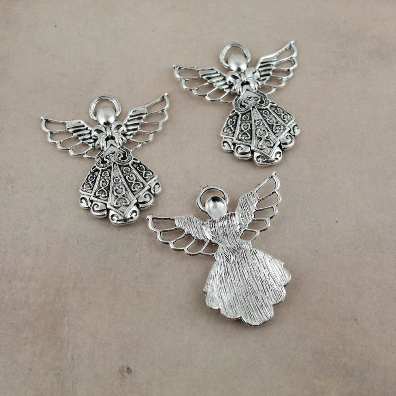 Pu&ograve; includere: Tre ciondoli a forma di angelo in argento con disegni intricati. Gli angeli hanno le ali e indossano abiti. I ciondoli sono perfetti per la creazione di gioielli o lo scrapbooking.