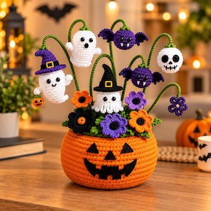 Op de afbeelding: Een gehaakt Halloween-arrangement met een grote oranje pompoenbasis met een jack-o'-lantern-gezicht. Het bevat diverse gehaakte figuren op groene stelen, waaronder spoken, paarse vleermuizen, een schedel en oranje, zwarte en paarse bloemen.