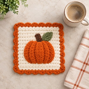 Puede incluir: Un posavasos cuadrado de ganchillo con un centro de color crema y una aplicación de calabaza naranja texturizada en el medio. La calabaza tiene un tallo marrón y una hoja verde. El posavasos está rematado con un borde festoneado naranja.