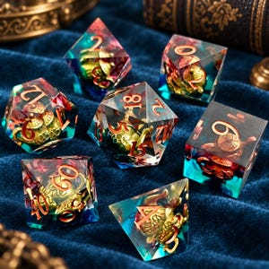 May include: A set of seven polyhedral dice made of clear resin with a blue and purple gradient tint. Each die contains a miniature gold-colored metal teapot figurine inside. The numbers on the faces are engraved in a metallic copper-toned finish.