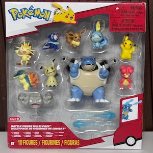 May include: A Pokemon Battle Figure Multi-Pack containing ten plastic character figures including Blastoise, Pikachu, Eevee, Meowth, Popplio, Sobble, Cyndaquil, Mimikyu, Geodude, and Magey, with two blue projectile accessories inside a clear plastic display box.