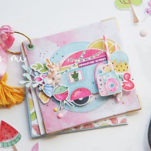 May include: A pink and blue scrapbook with a camper van, a flamingo, and a watermelon on the cover. The text "Wakacyjne Wyjazdy" is on the camper van.