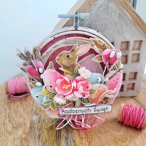 May include: A handmade Easter craft featuring a brown bunny rabbit surrounded by pastel pink, blue, and yellow eggs. The craft is decorated with flowers and greenery and includes the text "Radosnych Świąt" which translates to "Happy Holidays" in English.