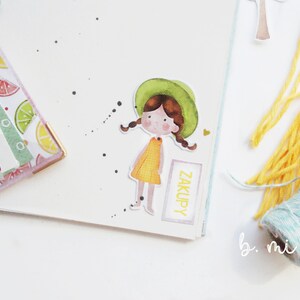 May include: A watercolor illustration of a girl with brown hair wearing a green hat and a yellow dress. The illustration is on a white background with black dots and the word "ZAKUPY" written on a pink rectangle.