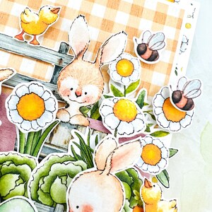 May include: A close-up of a handmade Easter card featuring two bunnies, a chick, and bees. The card has a gingham background and is decorated with flowers and greenery.