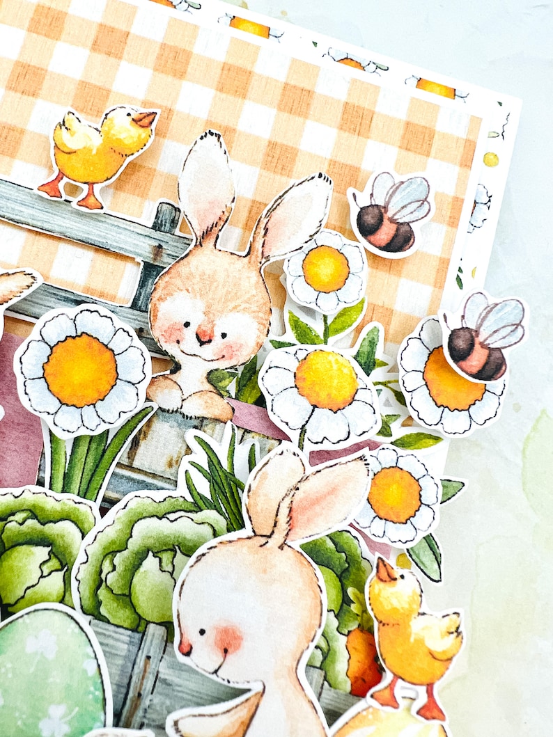 May include: A close-up of a handmade Easter card featuring two bunnies, a chick, and bees. The card has a gingham background and is decorated with flowers and greenery.