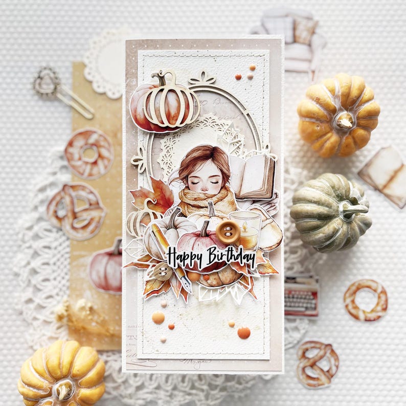 Op de afbeelding: Een handgemaakte kaart met een aquarel-illustratie van een meisje dat een boek leest met pompoenen en herfstbladeren. De kaart zegt "Happy Birthday".