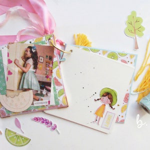 May include: A scrapbook with a colorful lemon and lime pattern, a photo of a girl, and a watermelon slice cutout. The scrapbook is decorated with pink ribbon, yellow yarn, and a small tree cutout. The scrapbook is open to a blank page with a sticker of a girl in a yellow dress and a green hat. The page also has the word "Happy" written on it.