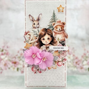 May include: A white card with a pink and white floral design. The card features a girl with brown hair, a bunny, a teddy bear, and a Christmas tree. The text "Urodzinki Hani" is written on the card.