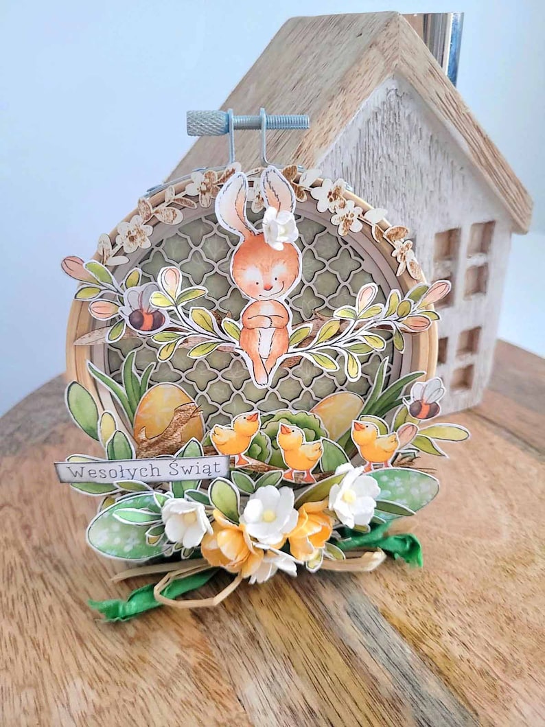 May include: A handmade Easter craft featuring a brown bunny rabbit sitting on a branch with green leaves and yellow flowers. The bunny is surrounded by yellow chicks and a sign that reads "Wesołych Świąt" which is Polish for "Happy Holidays".