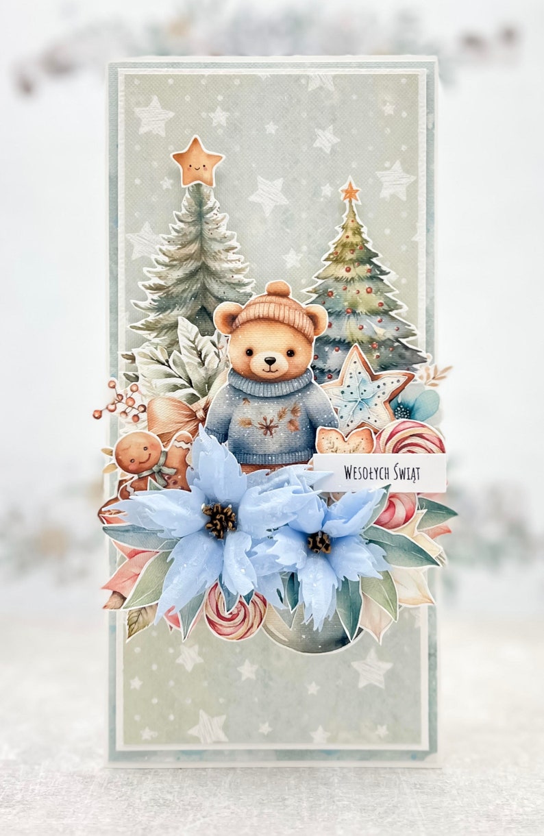 May include: A Christmas card featuring a teddy bear wearing a blue sweater and a Santa hat, standing in front of two Christmas trees. The card has a blue poinsettia, gingerbread man, candy canes, and a banner that reads "Wesołych Świąt" which means "Merry Christmas" in Polish.