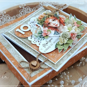 May include: A handmade card with a floral design and a girl's face. The card is open and has a small box inside. The card says "Martynie z okazji 10 urodzin" which translates to "Martynie for her 10th birthday".