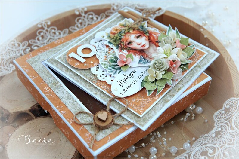 May include: A handmade card with a floral design and a girl's face. The card is open and has a small box inside. The card says "Martynie z okazji 10 urodzin" which translates to "Martynie for her 10th birthday".