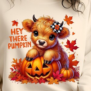 Puede incluir: Una vaca de las tierras altas de dibujos animados linda con un lazo blanco y negro se sienta encima de una calabaza de jack-o'-lantern. La vaca está rodeada de hojas de otoño y el texto "Hey there pumpkin" está escrito encima de la vaca.