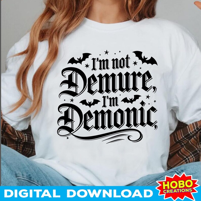 May include: White t-shirt with black text that reads "I'm not Demure, I'm Demonic" with bats and stars around the text.
