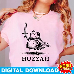 May include: Pink t-shirt featuring a black and white illustration of a frog wearing a cape and holding a sword. The word "Huzzah" is printed below the frog. The text "DIGITAL DOWNLOAD" is printed at the bottom.