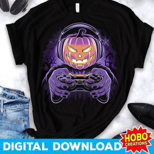 May include: A black t-shirt with a purple and orange jack-o'-lantern wearing headphones and holding a video game controller. The jack-o'-lantern has a spooky expression and is set against a dark background with a spider web and a spooky house.