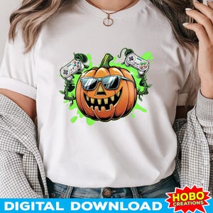 Op de afbeelding: Wit T-shirt met een groene, oranje en witte illustratie van een pompoen met een zonnebril en twee gamecontrollers.