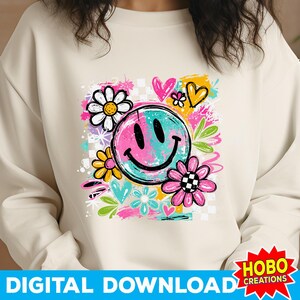 May include: Cream-colored sweatshirt featuring a colorful graphic of a smiley face split between pink and teal, surrounded by flowers, hearts, and abstract shapes. The words "DIGITAL DOWNLOAD" are at the bottom.