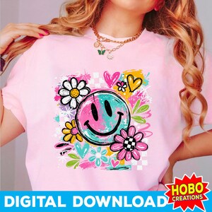 May include: Pink t-shirt with a colorful graphic featuring a smiley face, flowers, hearts, and the words "DIGITAL DOWNLOAD". The smiley face is split with pink and teal colors. The flowers are white, yellow, and pink. The design has a retro, groovy vibe.