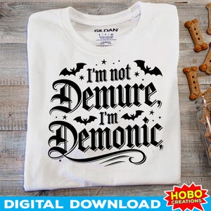 May include: White t-shirt with black text that reads "I'm not Demure, I'm Demonic" with bats and stars around the text.