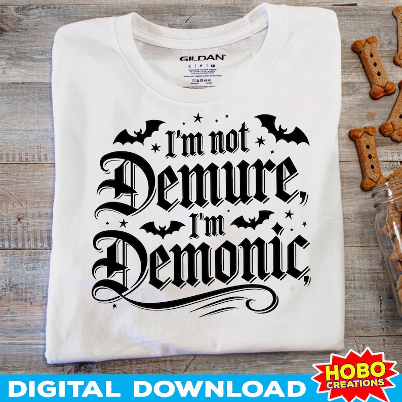 May include: White t-shirt with black text that reads "I'm not Demure, I'm Demonic" with bats and stars around the text.