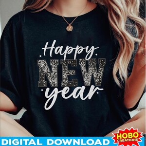 以下が含まれることがあります： 黒いTシャツに「Happy New Year」という文字が白いキラキラの文字で書かれています。このTシャツは、長いブロンドの髪をした人が着ています。