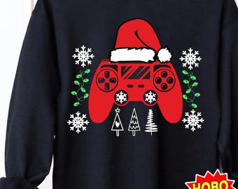 May include: A black sweatshirt with a red and white Christmas-themed video game controller design. The controller is wearing a Santa hat. The design includes snowflakes, Christmas lights, and Christmas trees.