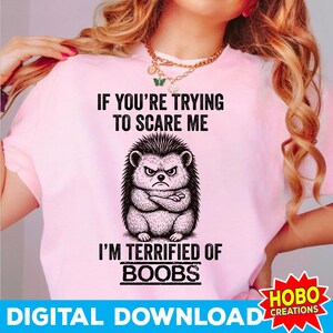 Könnte beinhalten: Hellrosa T-Shirt mit dem Text "IF YOU'RE TRYING TO SCARE ME I'M TERRIFIED OF BOOBS" und einer Grafik eines wütenden Igels. Das Shirt hat auch den Text "DIGITAL DOWNLOAD" und ein Logo.