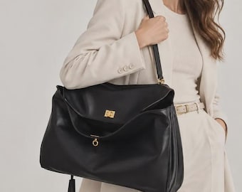 Peut inclure: Un grand sac à bandoulière en cuir noir doté d'un fermoir rotatif doré sur le rabat avant, d'un anneau doré assorti suspendu à la base et d'une bandoulière noire unique avec des attaches en métal doré.