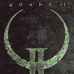 May include: A dark green and black graphic design featuring the word "QUAKE II" at the top. The central image is a stylized "II" with a circular element above. The "id" logo is in the lower left corner.