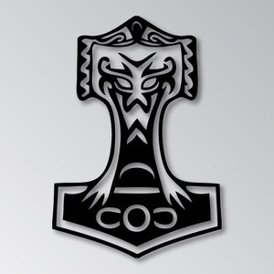 May include: Black metal wall art depicting Thor's hammer, Mjolnir, with intricate cut-out designs. The hammer features a stylized face and the letters "COS" at the base. A decorative piece for home or office.
