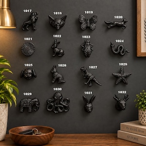 May include: A collection of black metal cabinet knobs shaped like animals and insects, labelled with numbers 1017 through 1032. The set includes a lion, fox, butterfly, rabbit, beetle, snake, dog, dinosaur, starfish, elephant, octopus, and deer head.
