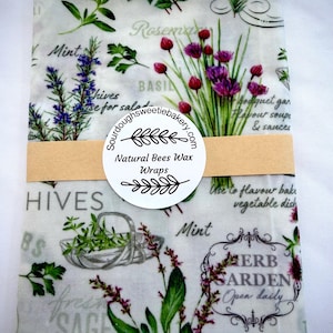 May include: A rectangular beeswax wrap featuring a botanical print of various herbs like rosemary, mint, and sage with text labels. A tan paper band wraps around the center with a circular sticker reading Sourdoughsweetiebakery.com Natural Bees Wax Wraps.