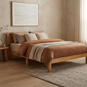 May include: A light-toned wooden bed frame featuring a headboard and a low-profile base. The bed is dressed in a rust-colored duvet, a light beige throw blanket, and several pillows in shades of brown, beige, and cream, creating a layered look.