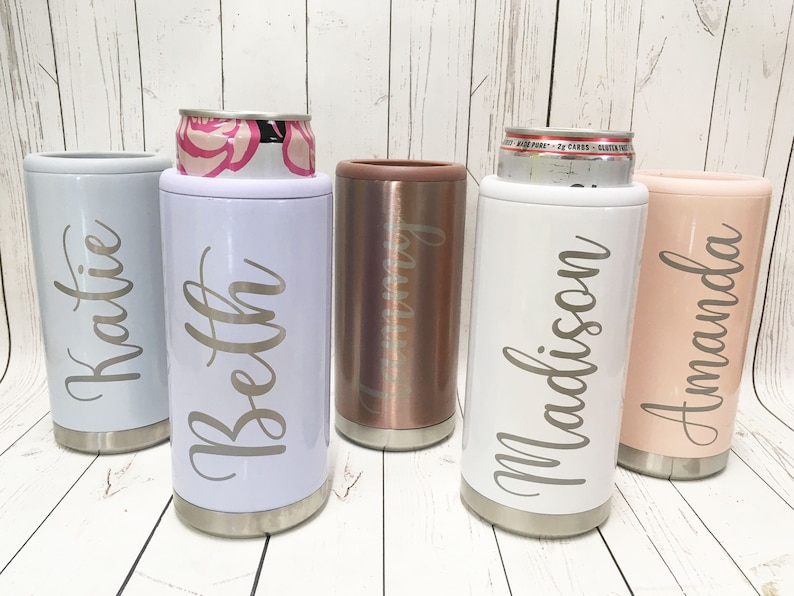 May include: Four personalized stainless steel can coolers in different colors. The coolers are labeled with the names "Katie", "Beth", "Madison", and "Amanda".