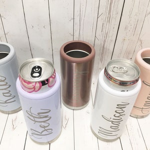 May include: Five personalized stainless steel can coolers. The coolers are in various colors, including gray, white, rose gold, and pink. Each cooler has a name engraved on it: Katie, Beth, Madison, and Amanda.