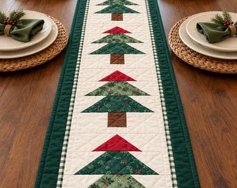 May include: A rectangular quilted table runner featuring a central row of four appliqued Christmas trees. Each tree has a brown trunk, a green patterned foliage section, and a red triangular top. The runner has a cream center and green border.