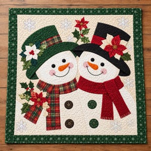 May include: A square quilted wall hanging featuring two snowmen with orange carrot noses and black button eyes. One snowman wears a green hat and plaid scarf, the other a black hat and red scarf. Both are decorated with poinsettias and snowflakes.