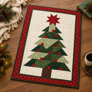 Op de afbeelding: Een rechthoekige gewatteerde wandhanger met een centraal kerstboomontwerp bestaande uit diverse groene stoffen driehoeken en kleine rode vierkantjes. De boom wordt bekroond met een rode ster en omlijst door een rode rand met een bloemmotief.