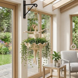 May include: A hanging planter featuring a ballerina figurine in a cream-colored leotard and ballet slippers. The figure holds a scalloped, shell-shaped bowl that contains a lush green trailing plant. The planter is suspended by gold chains.