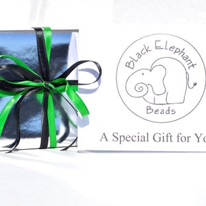 May include: A silver gift box tied with black and green ribbons. A card with the text "Black Elephant Beads" and a drawing of an elephant is next to the box. The card also reads "A Special Gift for You!"