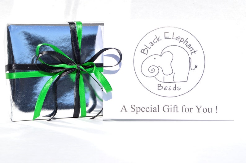 May include: A silver gift box tied with black and green ribbons. A card with the text "Black Elephant Beads" and a drawing of an elephant is next to the box. The card also reads "A Special Gift for You!"