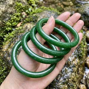 May include: A set of four smooth, circular bangles in a deep, solid forest green color. Each bangle features a polished, glossy finish with a rounded profile, creating a uniform appearance across the stack of four individual jewelry pieces.